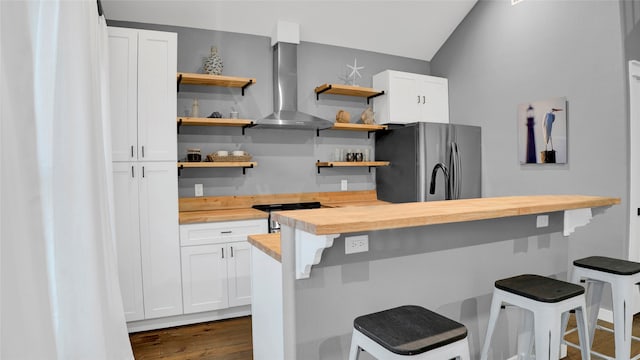 kitchen featuring a kitchen breakfast bar, wall chimney exhaust hood, dark hardwood / wood-style flooring, stainless steel appliances, and butcher block counters