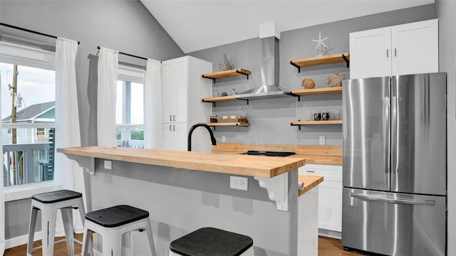 kitchen with stainless steel refrigerator, butcher block counters, wall chimney exhaust hood, lofted ceiling, and a breakfast bar area