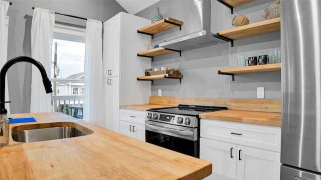 kitchen with wall chimney range hood, appliances with stainless steel finishes, white cabinetry, and wooden counters