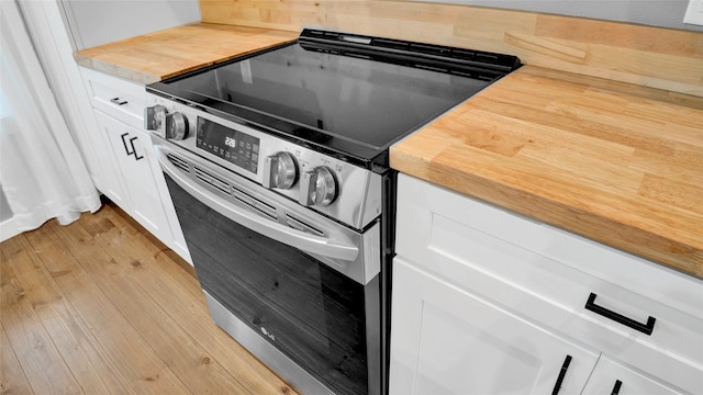 interior details with light wood finished floors, butcher block countertops, stainless steel range with electric stovetop, and white cabinetry