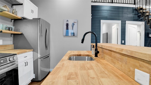 kitchen with sink, wood counters, white cabinetry, and stainless steel range with electric stovetop