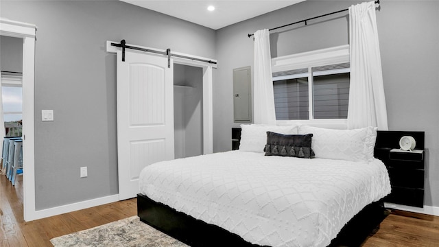 bedroom with recessed lighting, a closet, a barn door, wood finished floors, and baseboards