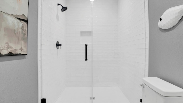 bathroom with a textured wall, a shower stall, and toilet