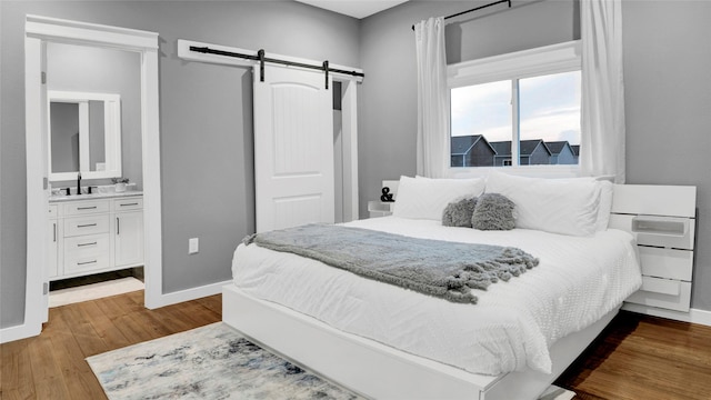 bedroom featuring a barn door, dark wood-type flooring, a sink, and baseboards