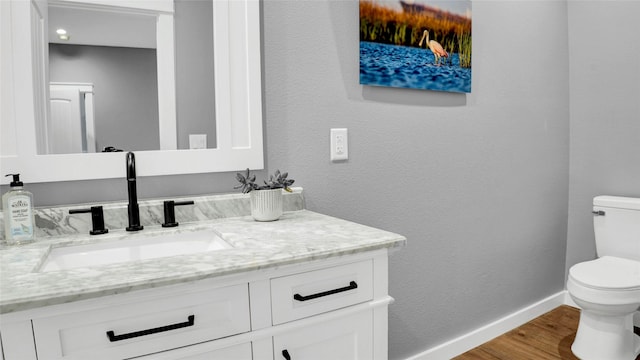 half bath featuring a textured wall, toilet, vanity, wood finished floors, and baseboards