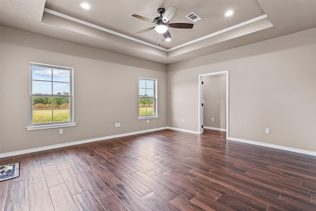 empty room with dark wood-type flooring, ceiling fan, a raised ceiling, and crown molding