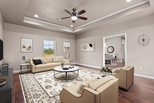 living room with a raised ceiling, ceiling fan, and dark wood-type flooring