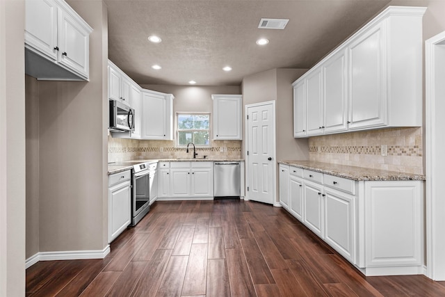 kitchen with dark hardwood / wood-style flooring, light stone countertops, appliances with stainless steel finishes, and white cabinets