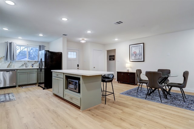 kitchen with a breakfast bar area, gray cabinetry, light hardwood / wood-style flooring, appliances with stainless steel finishes, and a center island