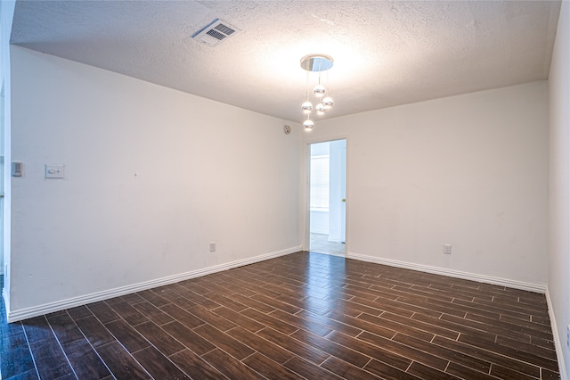 spare room with a textured ceiling, dark hardwood / wood-style floors, and an inviting chandelier