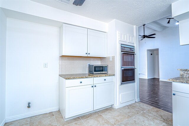 kitchen featuring white cabinets, light stone counters, double oven, ceiling fan, and tasteful backsplash