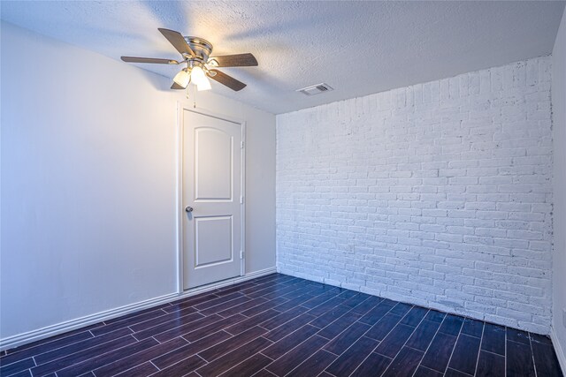 unfurnished room with dark wood-type flooring, ceiling fan, brick wall, and a textured ceiling