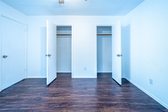 unfurnished bedroom featuring a textured ceiling, ceiling fan, dark hardwood / wood-style floors, and multiple closets