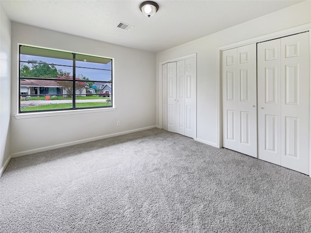 unfurnished bedroom featuring two closets and carpet