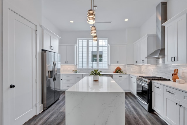 kitchen with appliances with stainless steel finishes, white cabinetry, wall chimney exhaust hood, pendant lighting, and a kitchen island