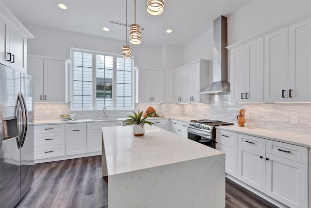 kitchen with pendant lighting, stainless steel appliances, a kitchen island, white cabinets, and wall chimney range hood