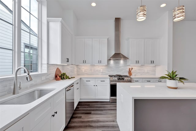 kitchen featuring sink, light stone countertops, appliances with stainless steel finishes, white cabinets, and wall chimney range hood