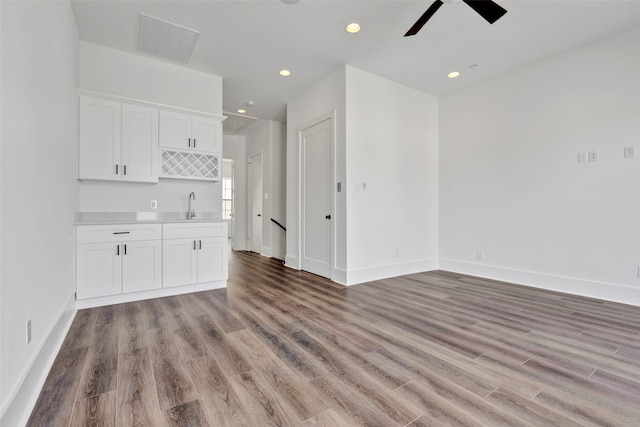 unfurnished living room with ceiling fan, sink, and wood-type flooring