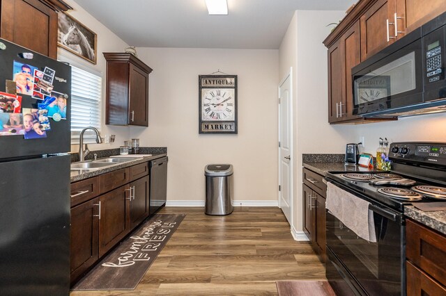 kitchen with black appliances, dark stone countertops, sink, and dark hardwood / wood-style flooring