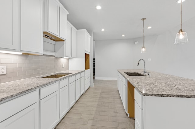 kitchen featuring light stone counters, a center island with sink, pendant lighting, sink, and white cabinets