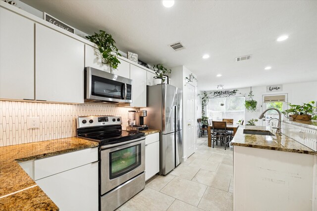 kitchen with white cabinets, dark stone countertops, stainless steel appliances, and sink