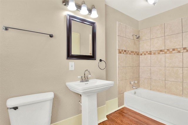 bathroom with hardwood / wood-style floors, toilet, and tiled shower / bath combo