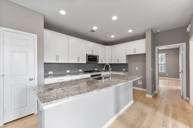 kitchen featuring light wood-type flooring, a center island with sink, white cabinetry, and sink