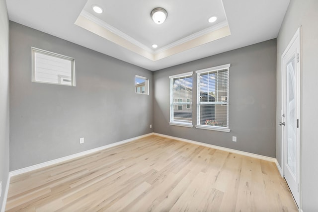 empty room featuring crown molding, a tray ceiling, and light hardwood / wood-style floors