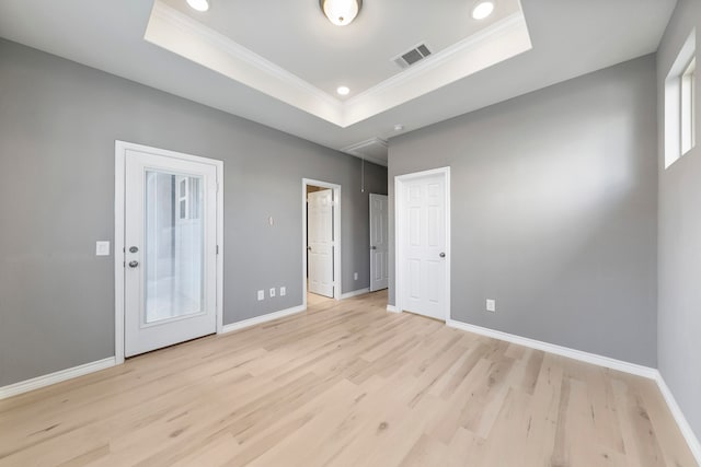 spare room featuring crown molding, a raised ceiling, and light wood-type flooring