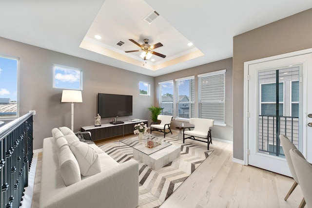 living room with a raised ceiling, ceiling fan, and light wood-type flooring