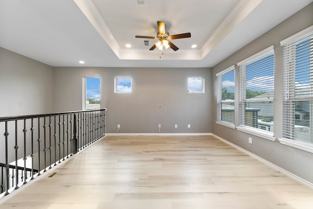 spare room featuring light hardwood / wood-style flooring, ceiling fan, ornamental molding, and a tray ceiling