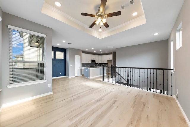 unfurnished living room featuring a tray ceiling, ornamental molding, ceiling fan, and light hardwood / wood-style floors