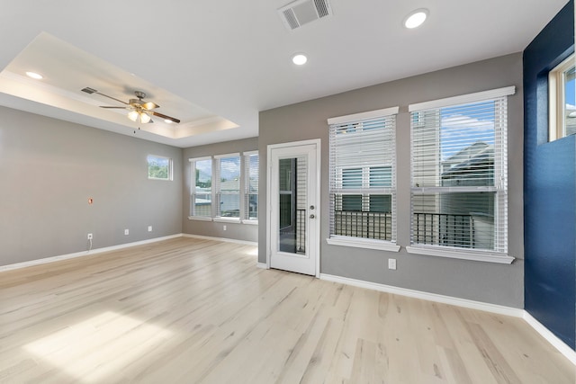 empty room with ceiling fan, a tray ceiling, and light hardwood / wood-style floors