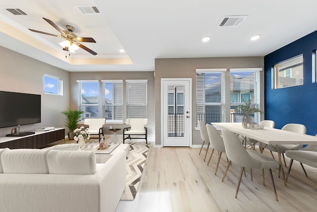 living room with a raised ceiling, ceiling fan, and light hardwood / wood-style floors