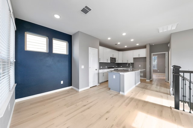 kitchen with a center island with sink, a healthy amount of sunlight, light hardwood / wood-style flooring, and white cabinets