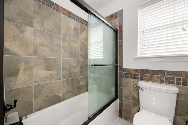 bathroom featuring tile walls, toilet, and bath / shower combo with glass door