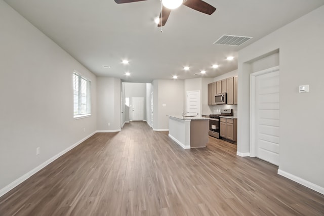 kitchen with hardwood / wood-style floors, appliances with stainless steel finishes, light stone counters, ceiling fan, and a kitchen island with sink