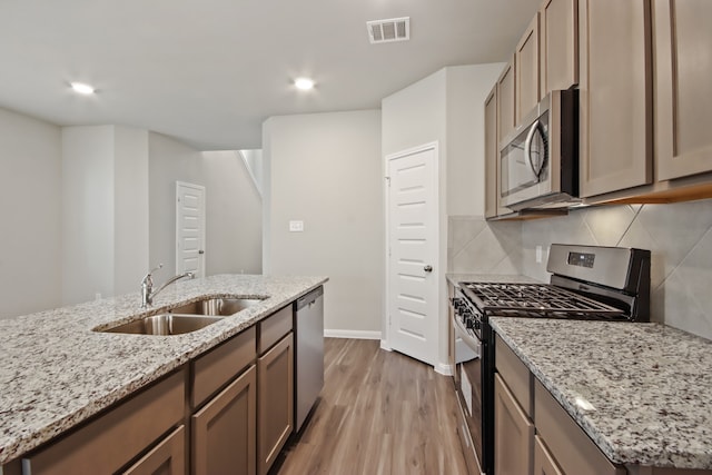 kitchen with light stone countertops, stainless steel appliances, sink, and light hardwood / wood-style flooring