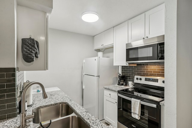 kitchen featuring appliances with stainless steel finishes, sink, white cabinetry, light stone counters, and decorative backsplash