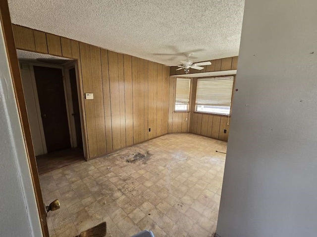 unfurnished room featuring wood walls, ceiling fan, and a textured ceiling