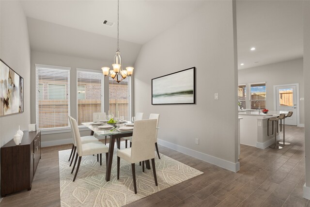 dining space featuring dark wood-type flooring, an inviting chandelier, a wealth of natural light, and vaulted ceiling