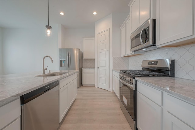 kitchen featuring stainless steel appliances, hanging light fixtures, white cabinets, light stone counters, and sink