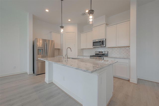 kitchen with white cabinets, decorative light fixtures, stainless steel appliances, sink, and a center island with sink