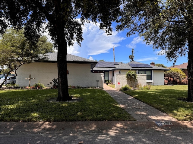 ranch-style house featuring decorative driveway, roof mounted solar panels, a front lawn, and an attached garage