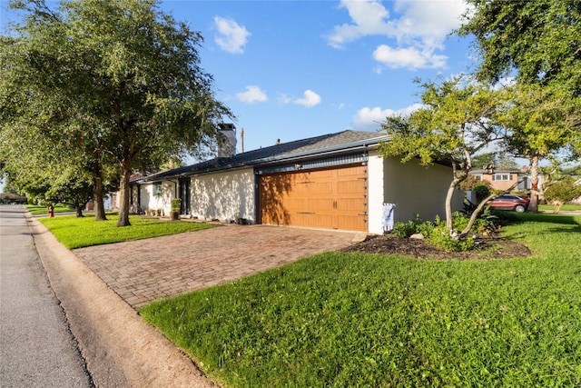 view of home's exterior featuring a yard, a chimney, decorative driveway, and a garage