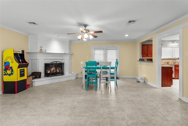 dining space featuring visible vents, a ceiling fan, crown molding, baseboards, and a brick fireplace