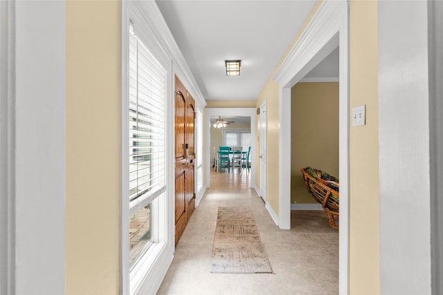 corridor featuring crown molding, light colored carpet, and baseboards