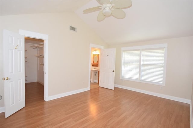 unfurnished bedroom with light wood-type flooring, lofted ceiling, a walk in closet, a closet, and ceiling fan