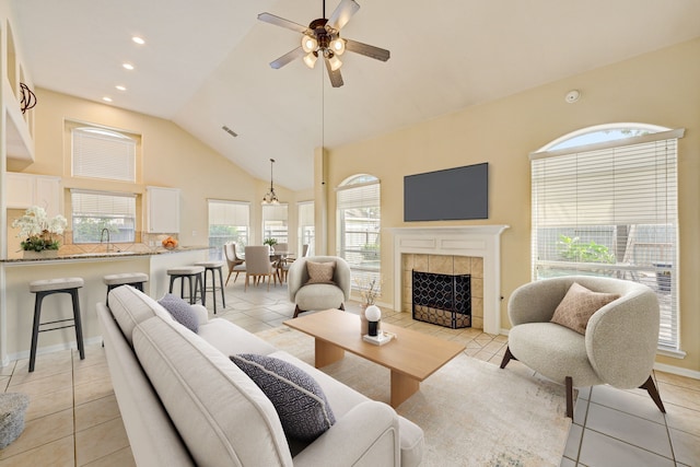 living room with light tile patterned floors, ceiling fan, high vaulted ceiling, a fireplace, and sink