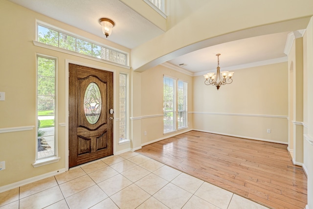 tiled entryway featuring an inviting chandelier and crown molding